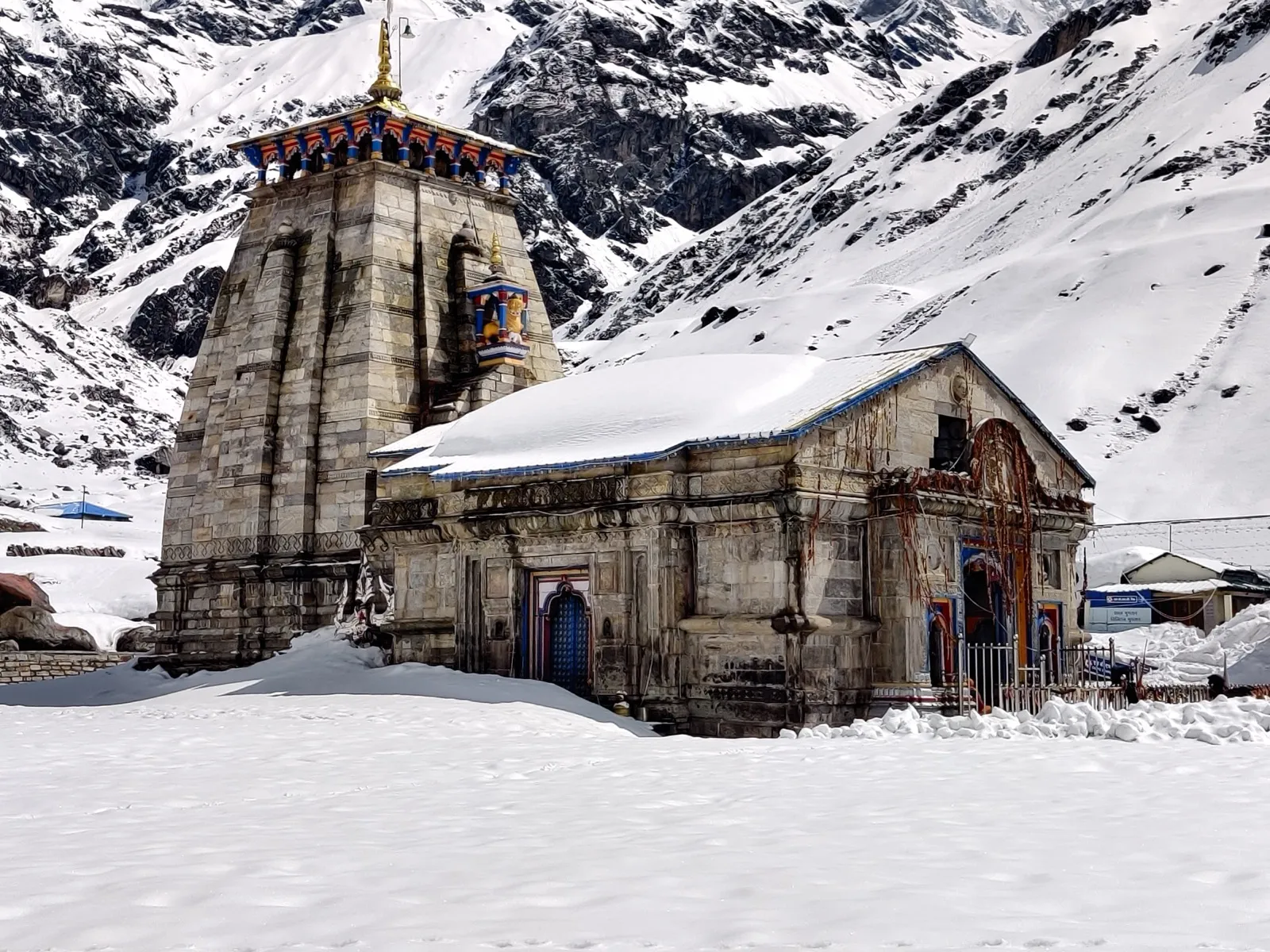 Kedarnath temple in winter, roof and forecourt buried under deep snow, with snow-covered slopes rising behind it and no pilgrims present